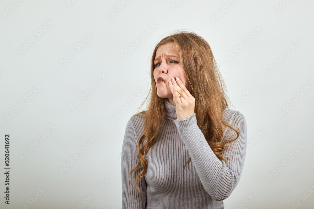 a young beautiful red haired woman in gray sweater suffers tooth pain through toothache makes hold hand on cheek a young beautiful red haired woman in gray sweater suffers tooth pain through toothache makes hold hand on cheek