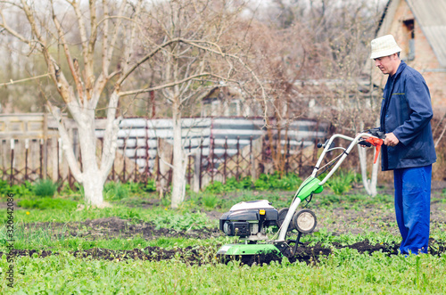 A man plows the land with a cultivator in a spring garden