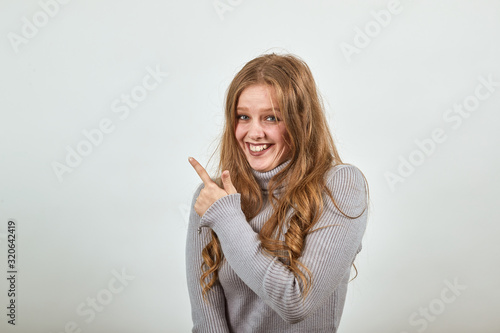 a young beautiful red-haired woman in a gray sweater smiles and points her index finger in the direction, happy and satisfied