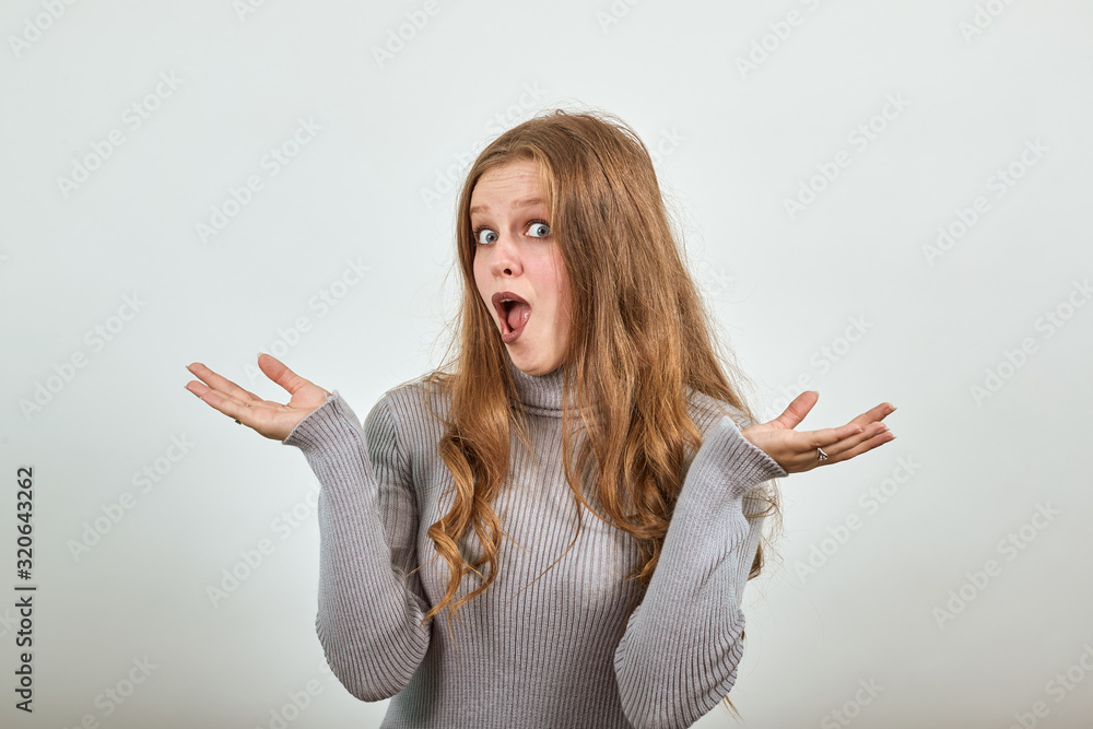 a young beautiful red haired woman in gray sweater with funny expression on face presents hands and looks surprised her mouth is slightly open a young beautiful red haired woman in gray sweater with funny expression on face presents hands and looks surprised her mouth is slightly open