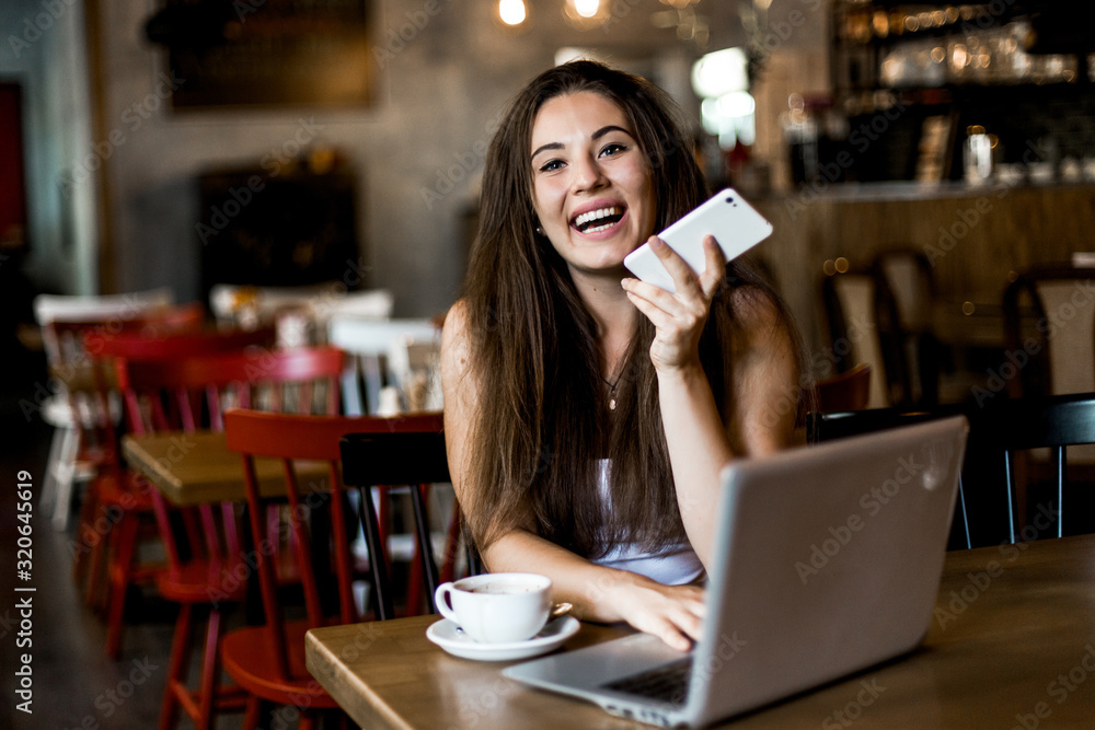 Business woman using phone, working on a laptop and drinking coffee in a cafe.