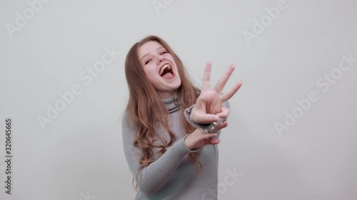 a young beautiful red haired woman in a gray sweater is happy showing three fingers and smiling with her mouth open