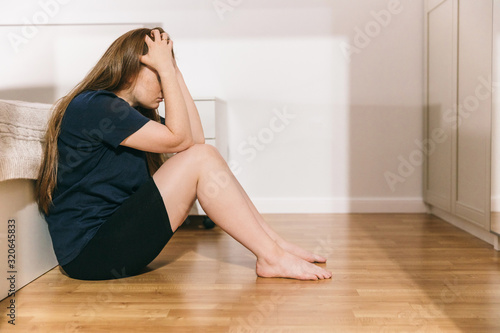 A married woman sits on the floor in the bedroom after a family quarrel, bruises on her body, signs of beatings. Domestic violence, abuse