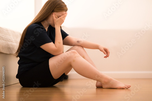 A married woman sits on the floor in the bedroom after a family quarrel, bruises on her body, signs of beatings. Domestic violence, abuse