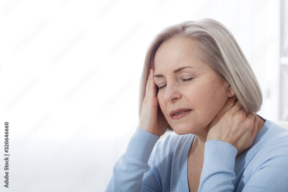 Woman suffering from stress or a headache grimacing in pain as she holds the back of her neck with her other hand to her temple, with copyspace. Concept photo with indicating location of pain. Woman suffering from stress or a headache grimacing in pain as she holds the back of her neck with her other hand to her temple, with copyspace. Concept photo with indicating location of pain.