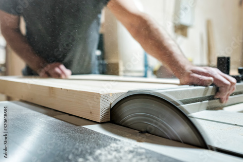 Obraz na płótnie Caucasian man carpenter cutting wood with circular saw creating new furniture