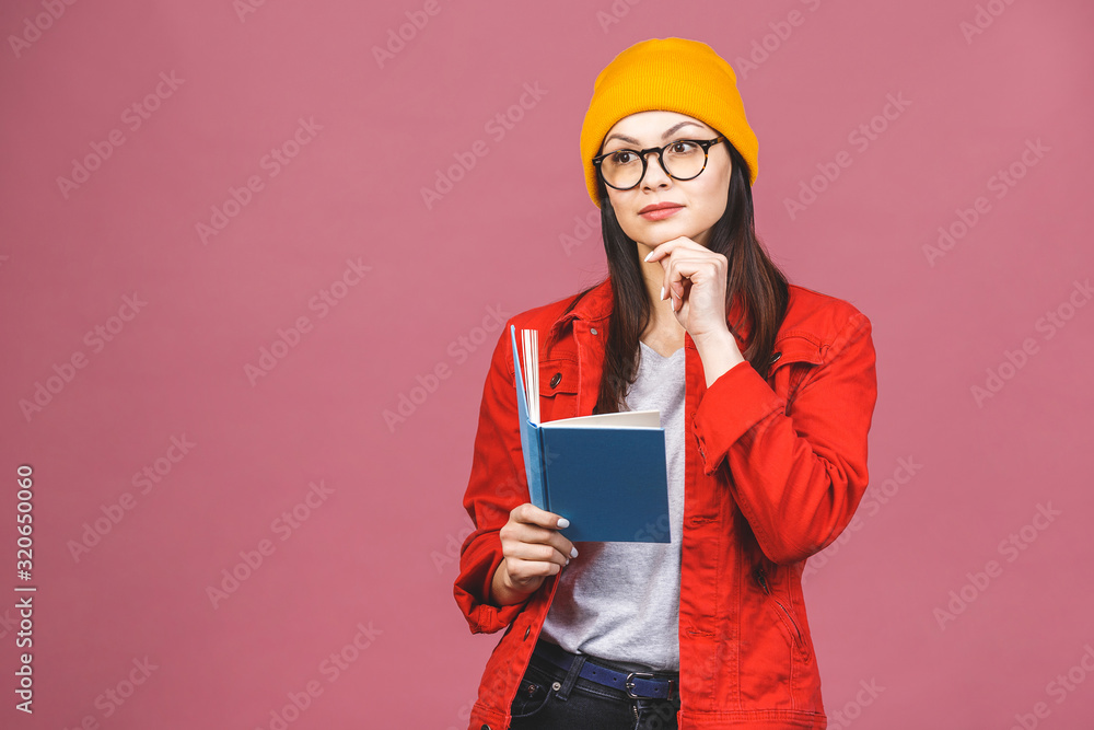 Beautiful young woman wearing casual and eyeglasses standing isolated over pink background, reading a book. Beautiful young woman wearing casual and eyeglasses standing isolated over pink background, reading a book.