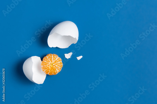 The concept of a broken egg, where instead of yolk peeled mandarin. Comic replacement of animal proteins with fruit. Funny veragatian breakfast. Substitution of objects based on shape and color. photo