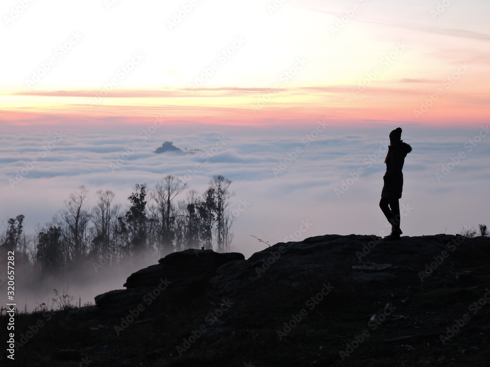 Lone female hiker contemplating the clouds from the top of a mountain