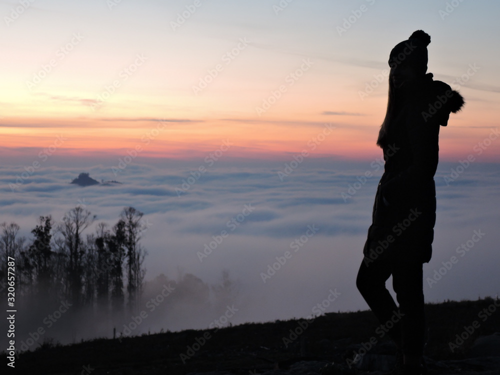 Lone female hiker contemplating the clouds from the top of a mountain