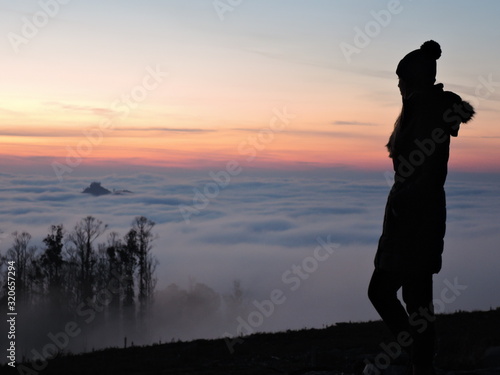 Lone female hiker contemplating the clouds from the top of a mountain