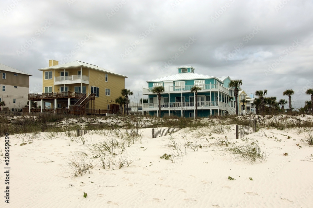 Travel America and visit Alabama background.Cloudy seascape with freshly built after hurricane colorful houses for vacation rentals and white sand in a foreground. Alabama Gulf Shores beach area, USA.