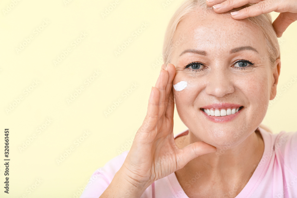 Beautiful mature woman applying facial cream against color background Beautiful mature woman applying facial cream against color background