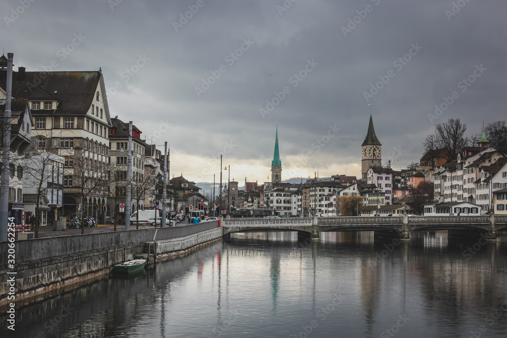 Cold and cloudy winter panorama of Zurich old town with Limmat river, bridges and St. Peter and Fraumunster church seen in the background.