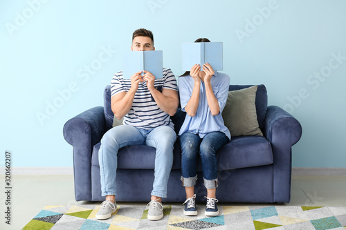 Young couple reading books while sitting on sofa at home