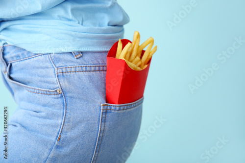 Young woman with french fries in pocket on color background, closeup