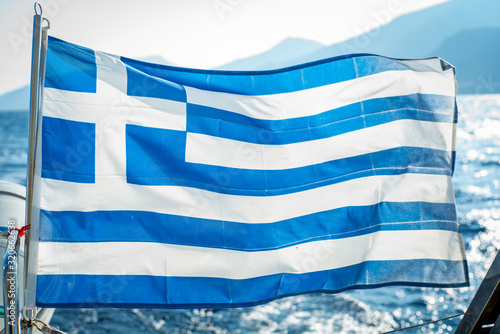 Greek flag flapping in wind from transom of boat in front of Greek Islands