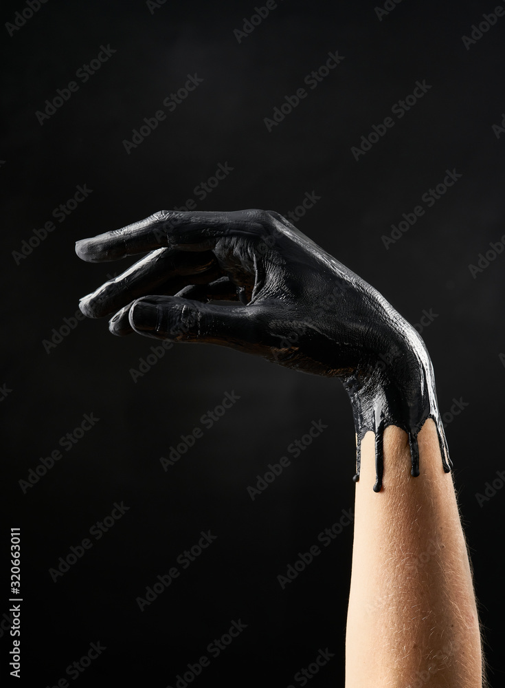 Female refined hand smeared with black acrylic paint on a black background
