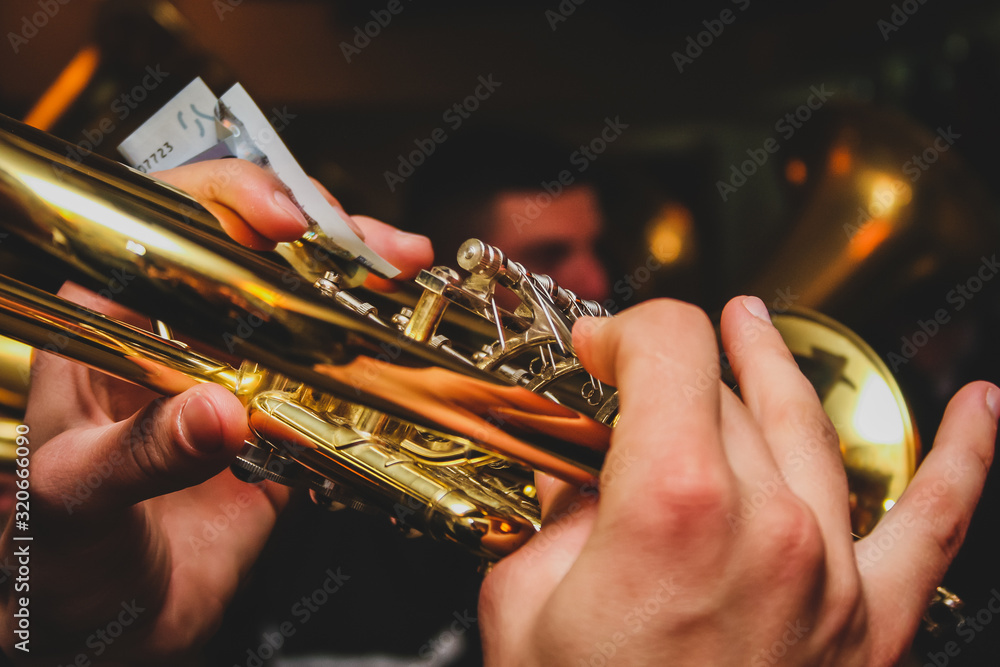 Obraz premium Detail of hands of a man playing on the trumpet while holding a euro note money bill. Concept of earning money with playing music with a band on different ocasions