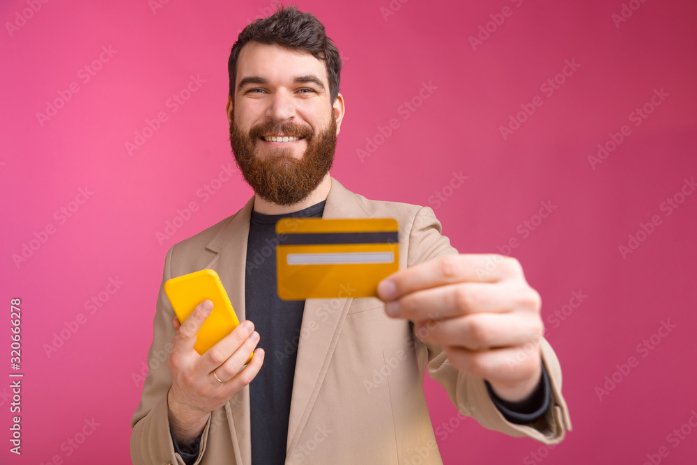 Portrait of smiling young man in suit holding smartphone and showing his credit card Portrait of smiling young man in suit holding smartphone and showing his credit card