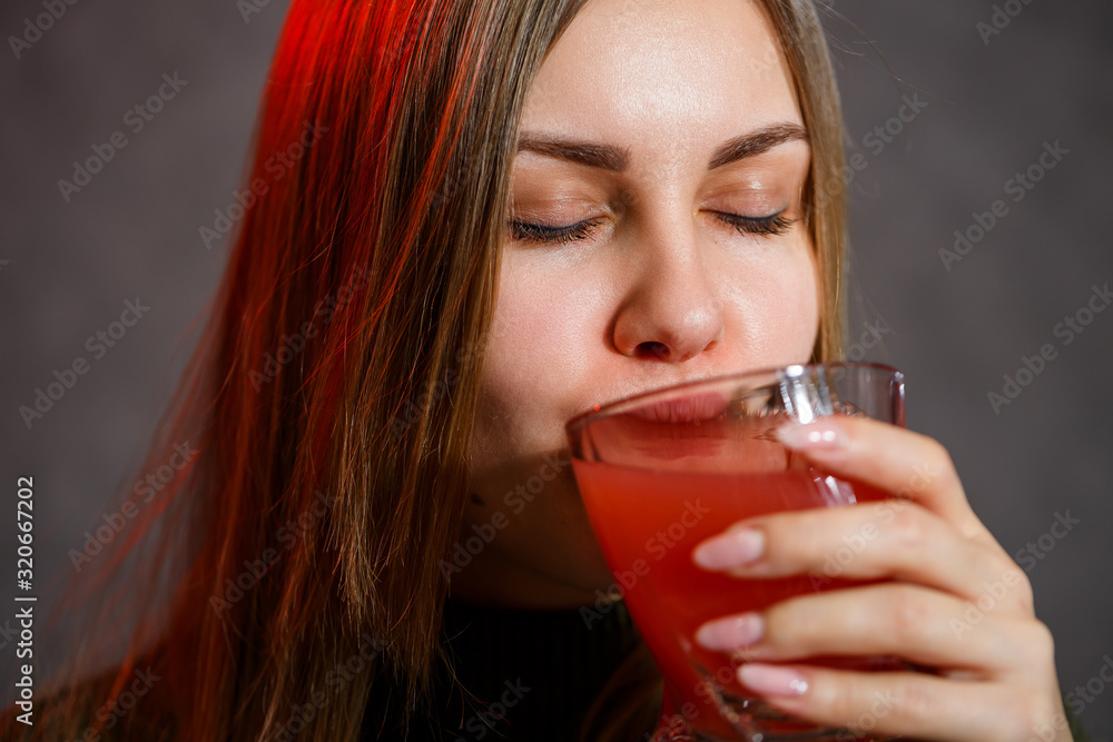 The girl is dressed in a green sweater and holds in her hands glassful with red and black liquid. The girl is dressed in a green sweater and holds in her hands glassful with red and black liquid.