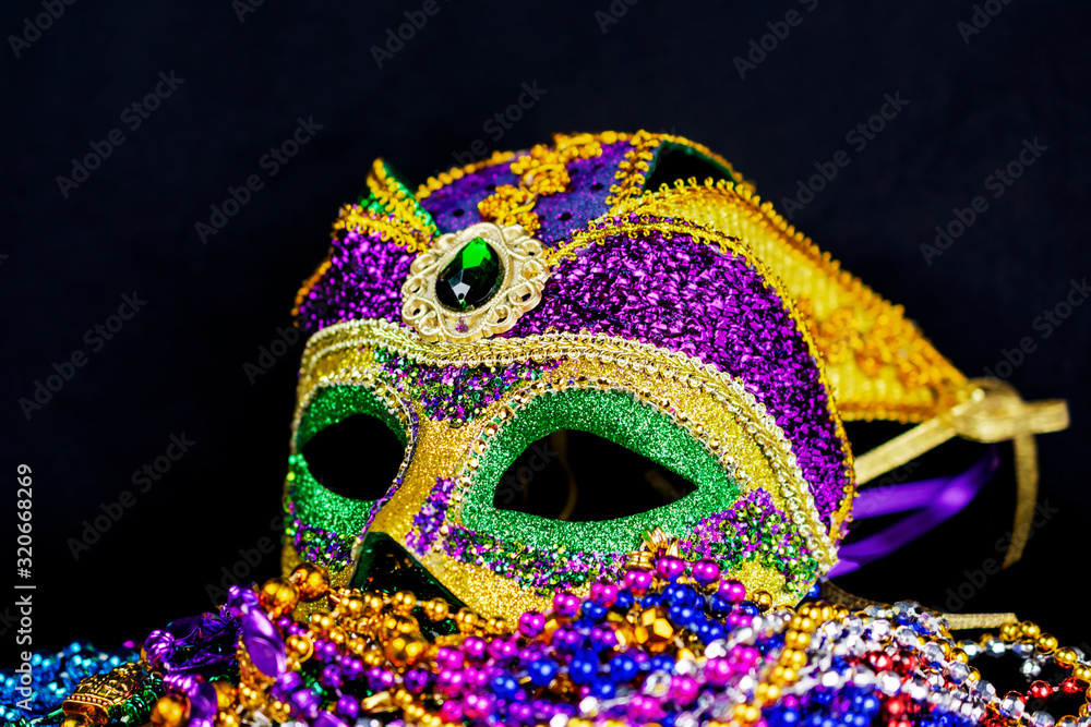 Jester mask on a bed of colorful beads.  Slightly side view.  Full mask with a black background.
