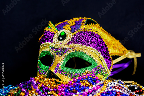 Jester mask on a bed of colorful beads.  Slightly side view.  Full mask with a black background. © Jennifer