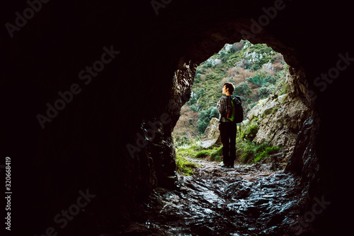 Young girl with backpack observes the landscape after going through a natural tunnel in the mountains. Concept of healthy life and adventures.
