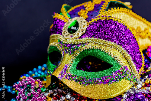 Close up view of a colorful jester mask on a bed of festival beads. Dark background. Landscape cropped.