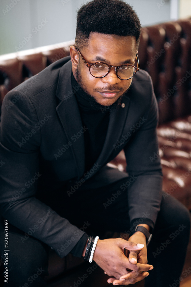 Portrait of an attractive african american man with glasses and stylish clothes sitting on a sofa Portrait of an attractive african american man with glasses and stylish clothes sitting on a sofa