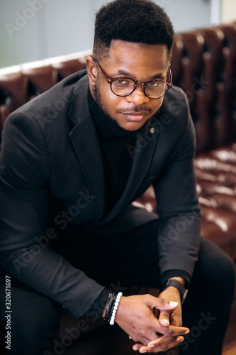 Portrait of an attractive african american man with glasses and stylish clothes sitting on a sofa