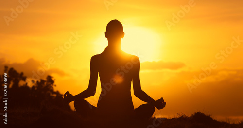 Female sitting on a hill meditating overlooking the golden sunset