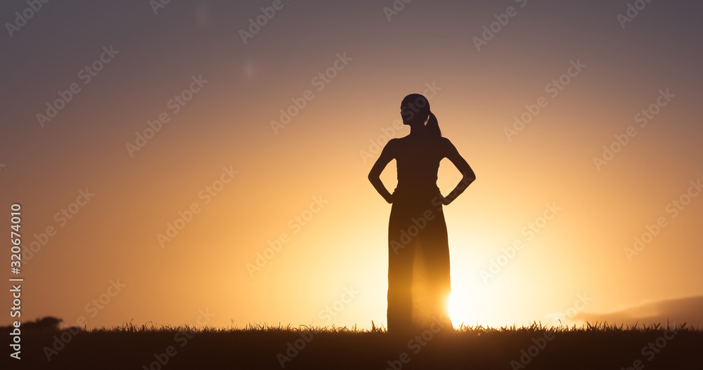 Female standing on a hill looking at the sunset. 