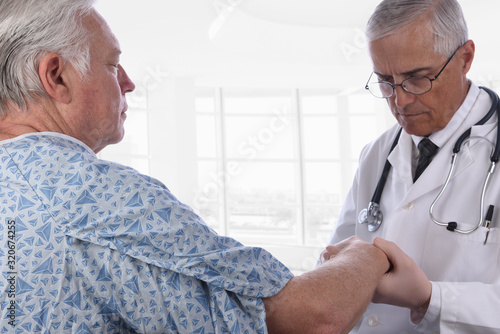 Closeup of a elderly male patient wearing a hospital gown as a doctor examines his right arm. Focus is on the patient.