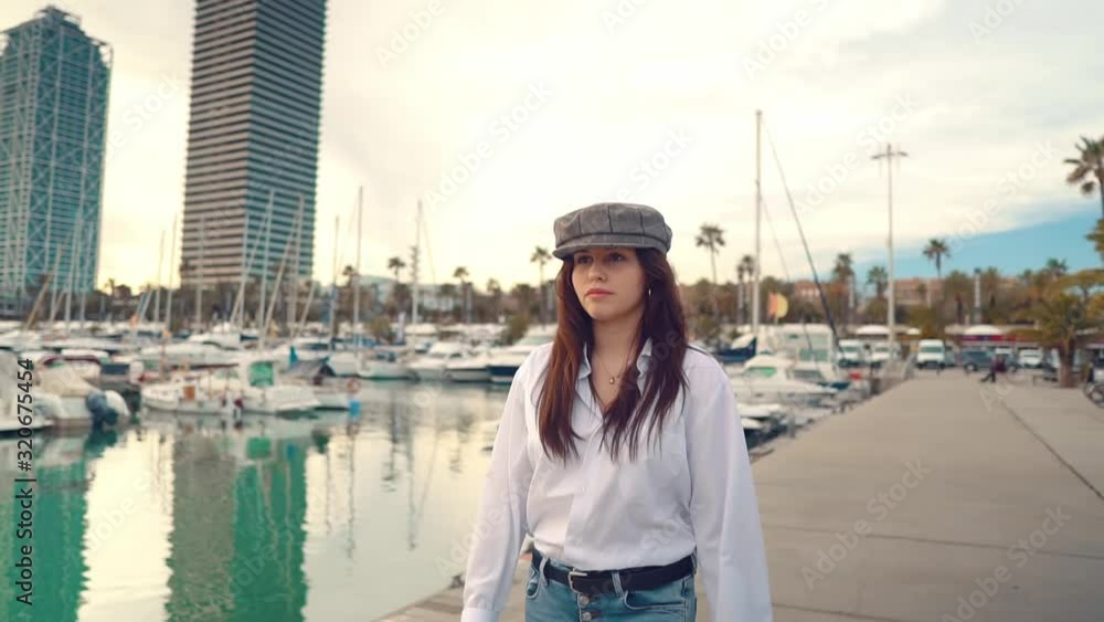 Portrait of young beautiful stylish woman in a white shirt and grey cap. She walks around the yacht club next to modern yachts. sea bay Portrait of young beautiful stylish woman in a white shirt and grey cap. She walks around the yacht club next to modern yachts. sea bay