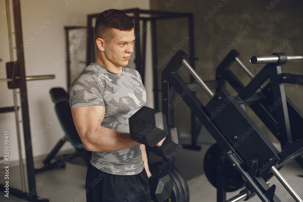 Sports man in the gym. A man performs exercises. Guy in a gray t-shirt Sports man in the gym. A man performs exercises. Guy in a gray t-shirt