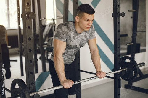 Sports man in the gym. A man performs exercises. Guy in a gray t-shirt