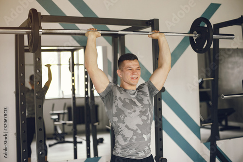 Sports man in the gym. A man performs exercises. Guy in a gray t-shirt