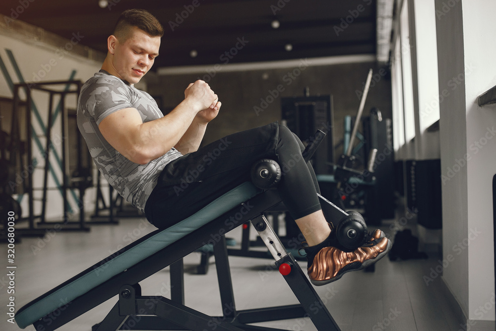 Obraz premium Sports man in the gym. A man performs exercises. Guy in a gray t-shirt