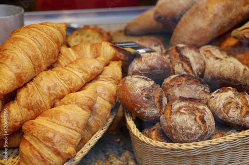 Heap and stack of round rye of rustic and crusty breads and butter croissants on wicker basket at display of bakery store. 
