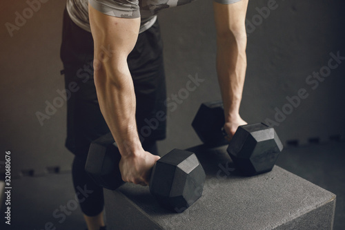 Sports man in the gym. A man performs exercises. Guy in a gray t-shirt
