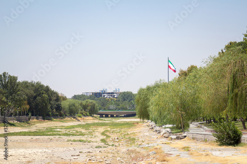 Flag of the Islamic Republic of Iran waiving in front of the Zayandeh river, dried due to the especially warm summer that provoked drought on the desertic climate and environment of Isfahan, Iran.