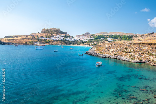 Boats anchored on sea near village of Lindos, Acropolis of Lindos in background (Rhodes, Greece)
