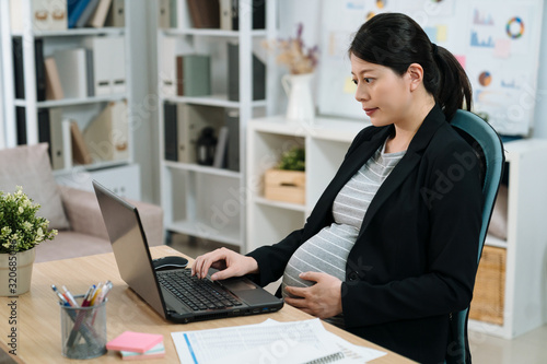 Canvas-taulu Pregnant asian chinese businesswoman in suit using laptop computer in modern office