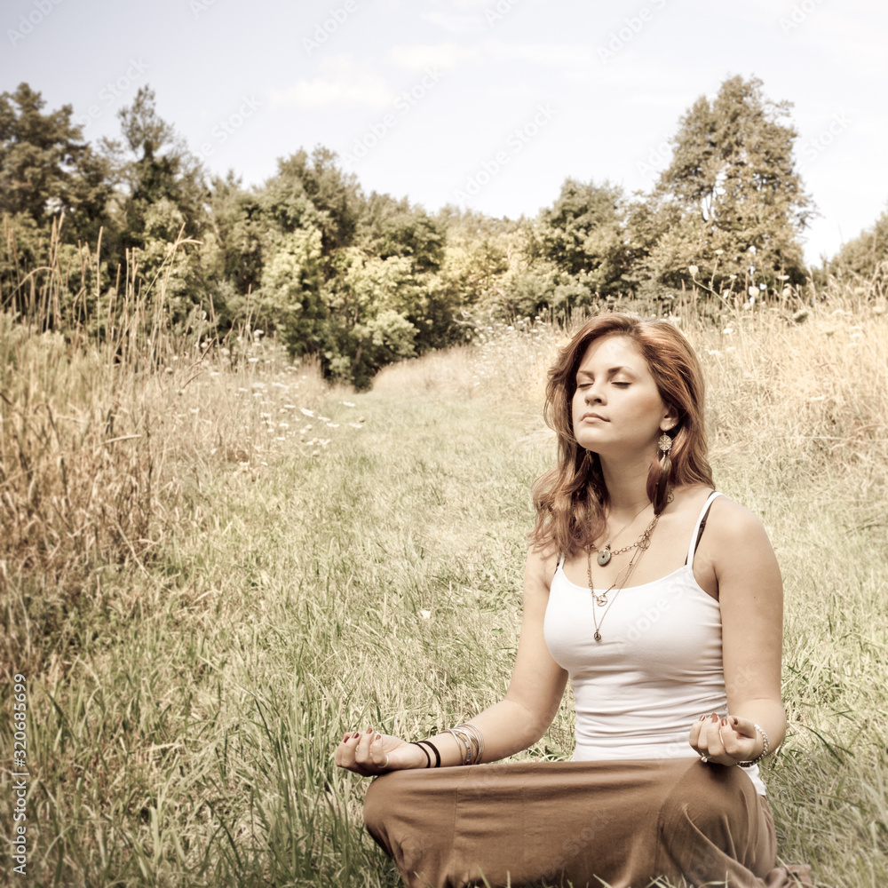 Young woman in lotus position in a sunny field