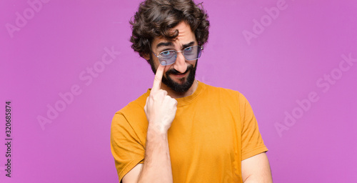 young crazy cool man keeping an eye on you, not trusting, watching and staying alert and vigilant against flat wall photo