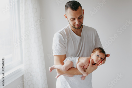 Happy Caucasian father holding newborn baby. Male bearded man parent rocking child daughter son in his hands. Authentic lifestyle candid moment. Young dad family life concept.