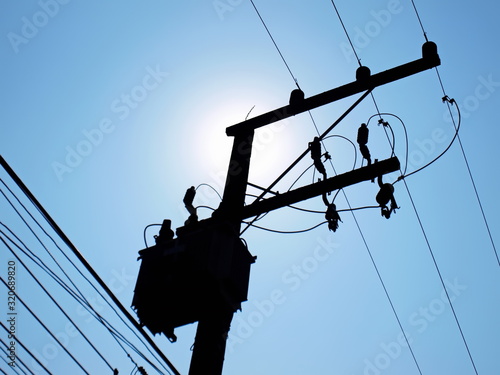 Silhouette of transformers and cables on poles. On a background of blue sky with light morning sun with space reproduction.