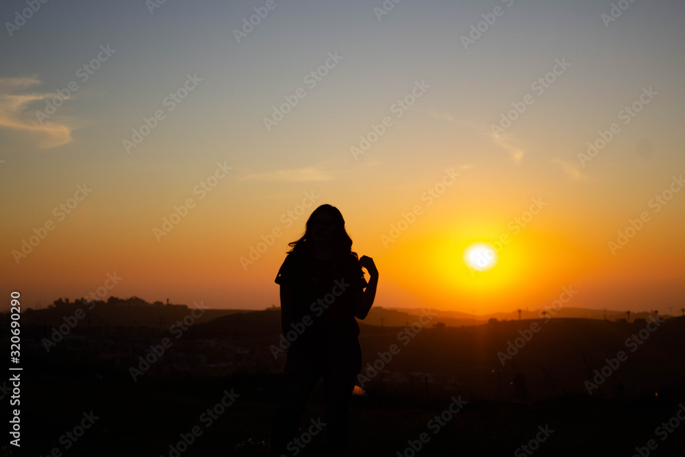 backlit silhouette of young woman posing in sunset of blue and red sky