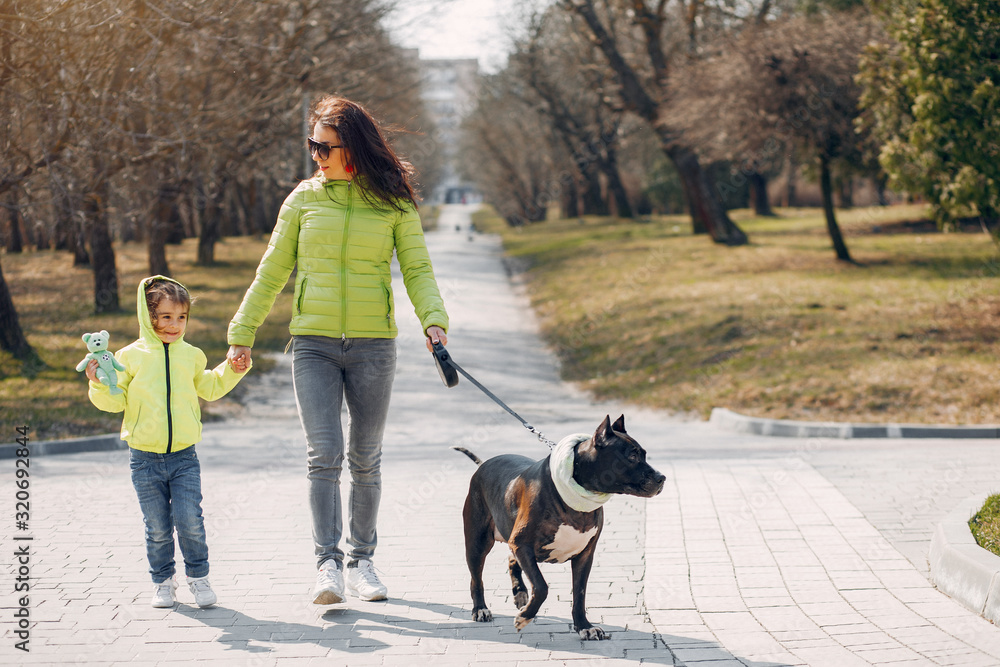Beautiful mother with daughter. Family in a spring park. Woman in a green jacket. Family with a big dog